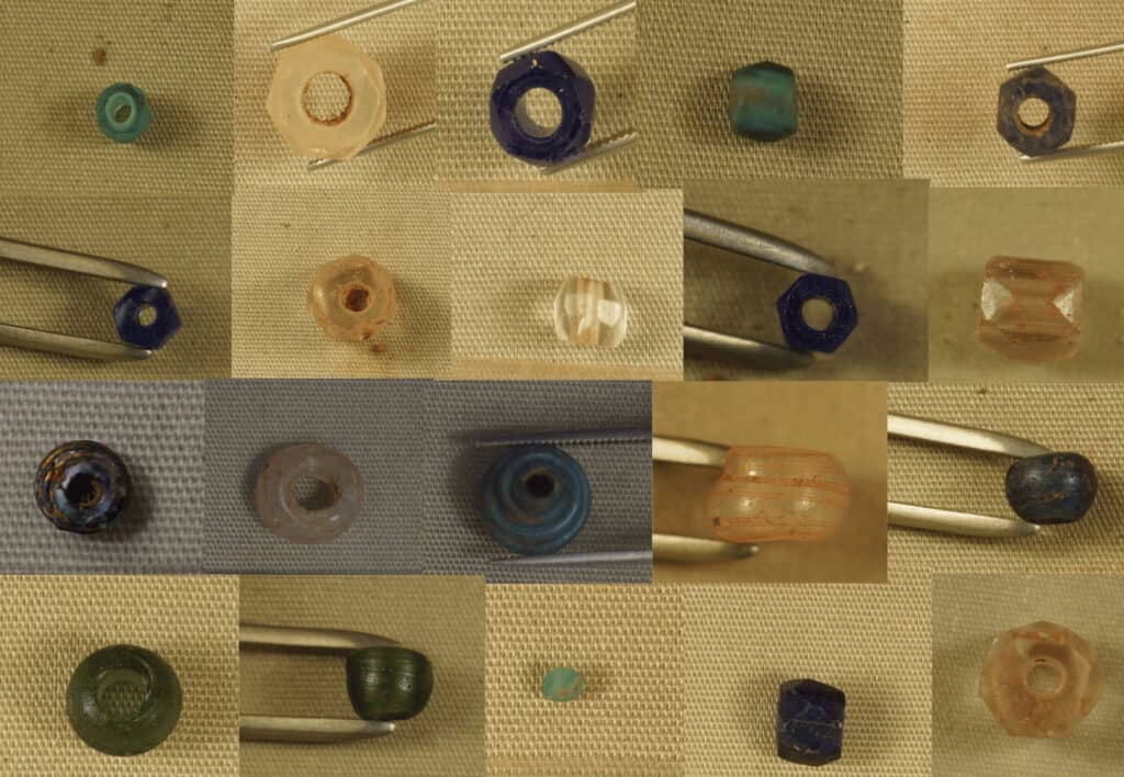 A grid of variously colored and shaped beads displayed on a textured background, with some held by metal tweezers for a detailed view.