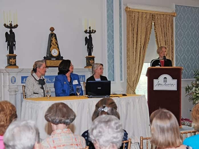 Gail Serfaty, Lynne Hastings, and Betty Monkman with Marge Grills at podium in Grand Salon of the Visitor Center William duPont Gallery.