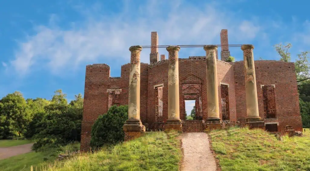 Ruins of an old brick structure with tall columns set against a blue sky and surrounded by greenery.