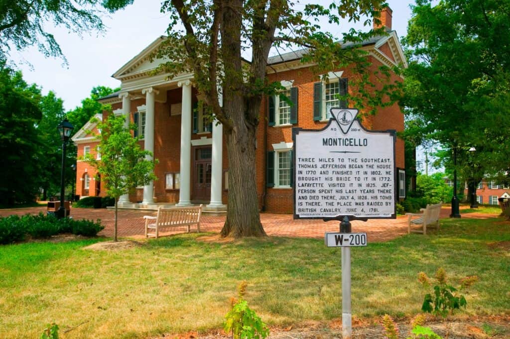 Monticello, Thomas Jefferson’s historic brick home in Virginia, with white columns, green shutters, and a roadside historical marker surrounded by trees and benches.