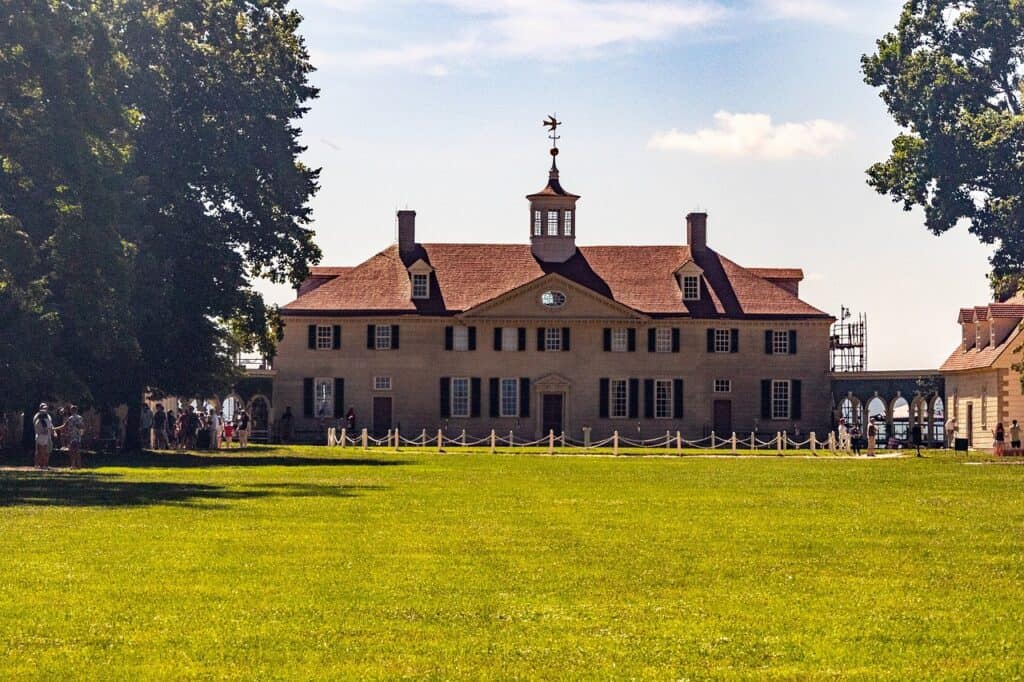 Mount Vernon estate with George Washington’s historic mansion overlooking a wide green lawn, featuring a red roof, central cupola, and visitors walking the grounds on a sunny day.