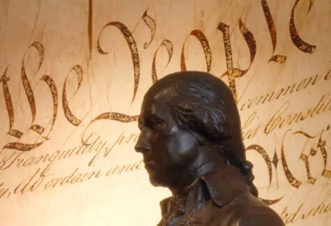 Bronze statue of James Madison in front of a large display of the U.S. Constitution’s “We the People” preamble text.