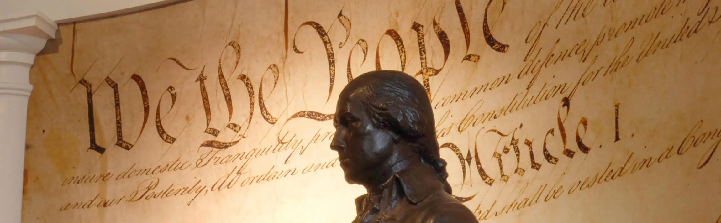 Bronze statue of James Madison in front of a large display of the U.S. Constitution’s “We the People” preamble text.