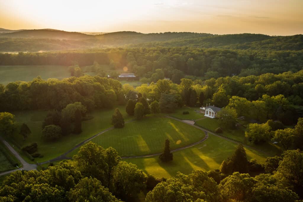 Aerial view of James Madison’s Montpelier estate surrounded by green fields and forested Virginia hills at sunset.